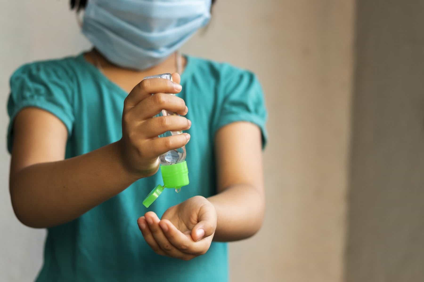 Child wearing medical face mask applies hand sanitizer