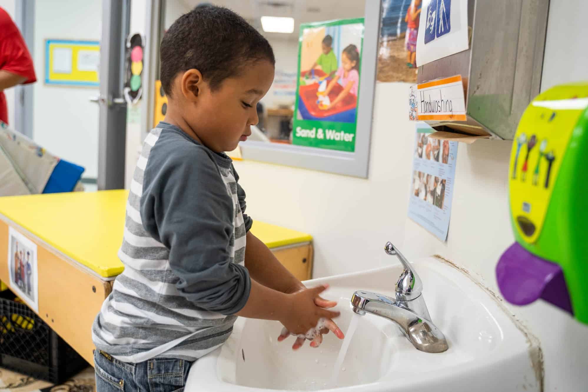 young child washing hands at sink