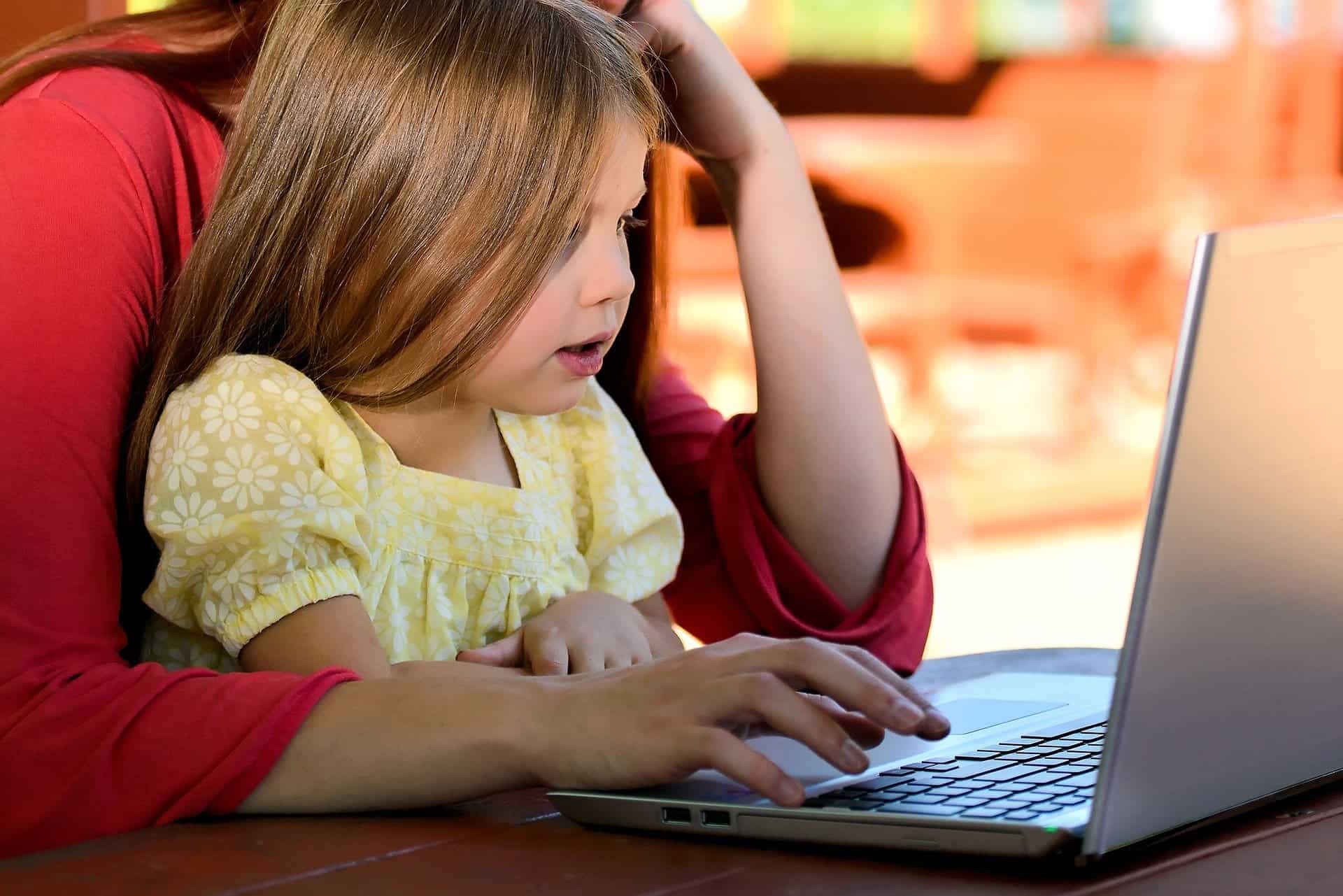 Young girl, about 6 years old, sits on a woman's lap in front of a laptop