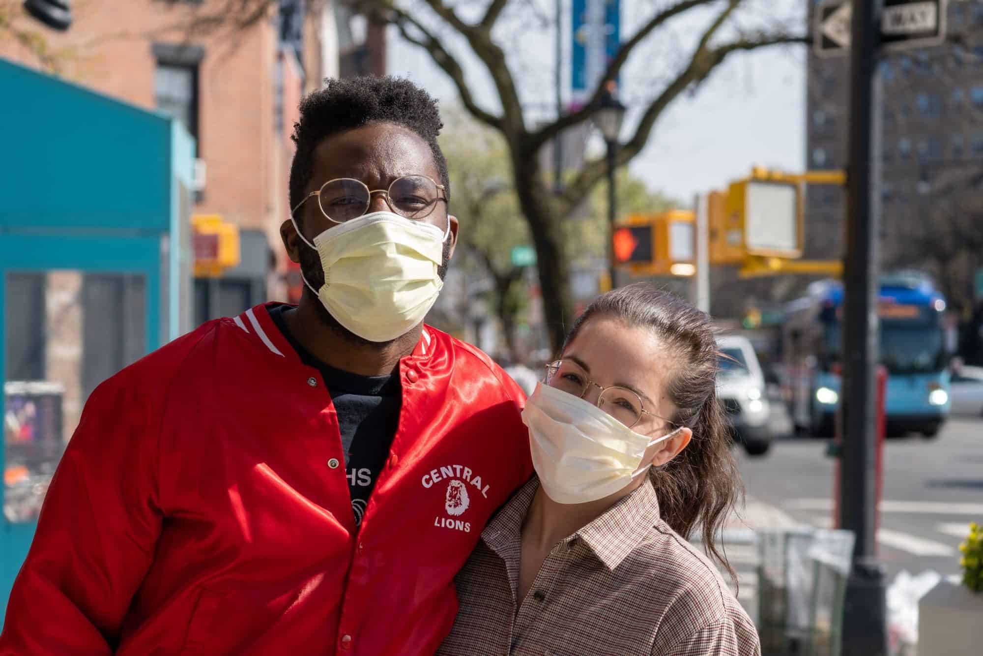 Two older students in medical facemasks pose together outside